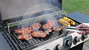 View of man cooking meat steak with corn on gas grill.