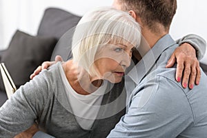 View of man embracing senior mother at home