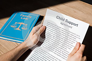 View of man holding document with child support agreement near family law book on desk