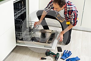 View Of Man In Overall Repairing Dishwasher In Kitchen