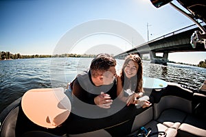 View of man and woman looking at each other while sitting on motorboat with surfboards nearby