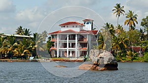 The view of mansion on the shore with palm trees. Action. Living at the sea shore with green vegetation.