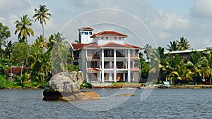 The view of mansion on the shore with palm trees. Action. Living at the sea shore with green vegetation.