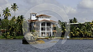 The view of mansion on the shore with palm trees. Action. Living at the sea shore with green vegetation.