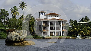 The view of mansion on the shore with palm trees. Action. Living at the sea shore with green vegetation.