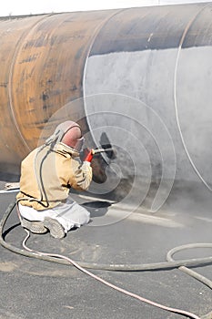 View of the manuel sandblasting to the large pipe. Abrasive blasting more commonly known as sandblasting is the operation.