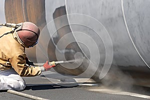View of the manuel sandblasting to the large pipe. Abrasive blasting more commonly known as sandblasting is the operation.