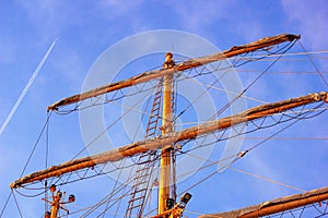 View of the masts and rigging of a sailing ship close-up against the background of sky with a flying airplane