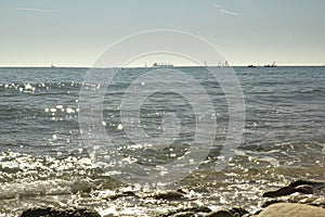 View of the Mediterranean Sea, waves. In the background are ships and sailboats. sunny day. large stones on the shore