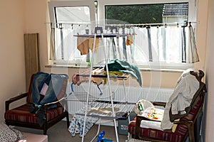 View of messy small room with laundry hanger and windows in cheap apartment