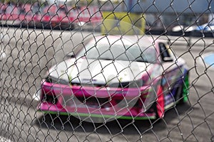 View through metal fence cage at blurred color racing car in parking