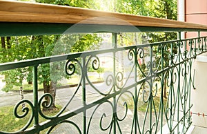 View from a modern balcony through a metal openwork wrought iron fence with railings to the Park on a Sunny summer day