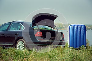 View of modern black car and suitcase on the river`s side