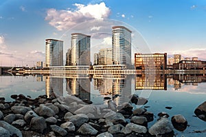 View of modern buildings on the river bank in the Moscow district with stones in the foreground and reflections in the water