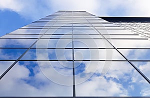 View of a modern glass skyscraper. Reflection of a cloudy blue sky in a glass skyscraper