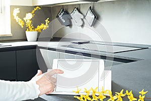 View of the modern kitchen. Mockup of a tablet with white blank screen over the kitchen table. Copy space. In the forsythia branch