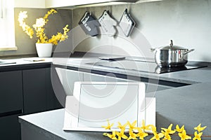 View of the modern kitchen. Mockup of a tablet with white blank screen over the kitchen table. Copy space. In the forsythia branch