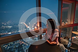 View of the modern metropolis at night. Bangkok, Thailand. The girl is enjoying a delicious cocktail at the bar on the 86th floor