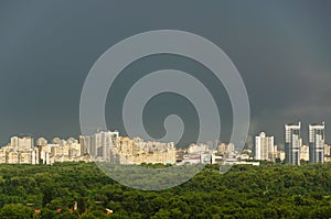 View of modern residential area against the gray cloudy sky after rain and lush foliage in summer. Left bank of Kyiv