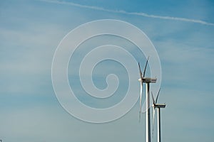 view of a modern windmill against a blue sky. The white blades of the wind turbine close up. Renewable energy source. Production
