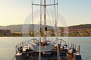 View of moored yacht. From the yacht`s deck to the bow and sails. Gear and equipment on the boat. City Koper in the background