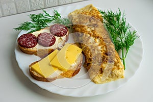 View of morning breakfast consisting of omlete and two sandwichessurrounded by fresh green dill on white plate