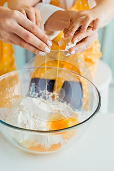View of mother and daughter smashing egg into bowl with flour