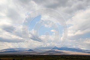 View of mount Ararat hidden by clouds which rises above the Ararat valley and stunning blue sky with low clouds