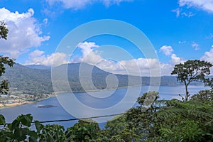 View from mountain ridge to Buyan lake on Bali island in Indonesia. Lush tropical vegetation and tall trees on a steep slope.