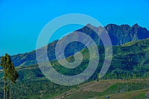 View of mountain ridges and sloping hills with trees under a clear blue sky