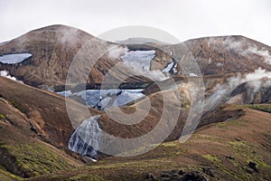 View mountain valley with snow, waterfall, moss and foggy hills. Laugavegur hiking trail, Iceland