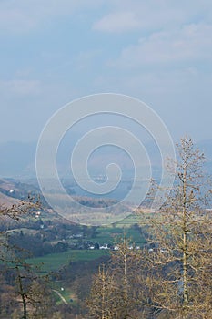 View from a mountain: between winter trees to a lake and hazy mountains English Lake District