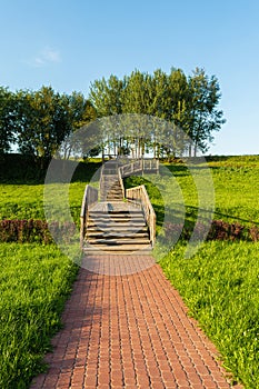 View of the multi-level wooden gangway in a picturesque place with a field and trees. Summer evening before sundown. Nature