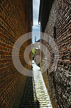 View on narrow alley in medieval belgian village with old brick stone walls on both sides, cobblestone street - Lier Begijnhof,