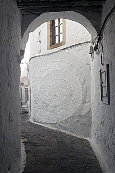 A view of a narrow street with arch and wooden windows and doors with white wall stone architecture of the island Patmos, Greece