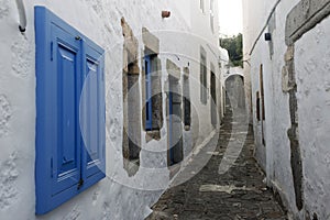 A view of a narrow street with arch and wooden windows and doors with white wall stone architecture of the island Patmos, Greece