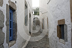 A view of a narrow street with arch and wooden windows and doors with white wall stone architecture of the island Patmos, Greece