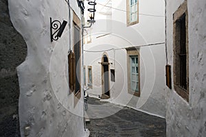 A view of a narrow street with arch and wooden windows and doors with white wall stone architecture of the island Patmos, Greece