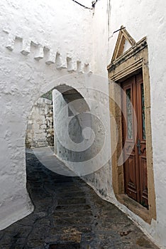 A view of a narrow street with arch and wooden windows and doors with white wall stone architecture of the island Patmos, Greece