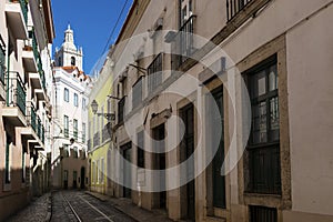 View of a narrow street and buildings with a tower of the Sao Vincente de Fora church on the backrgound, in the historic neighborh photo