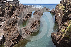 View of the natural pools on village of Porto Moniz, formed by volcanic rocks, islet of Mole in the background, coast of the