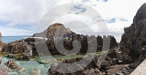 View of the natural pools on village of Porto Moniz, formed by volcanic rocks, islet of Mole in the background, coast of the