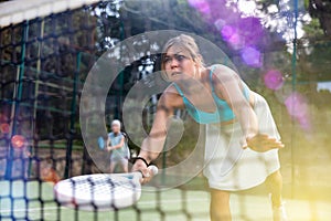 View through net of young female paddle tennis player hitting ball
