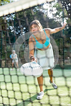 View through net of young woman playing paddle tennis on outdoor court