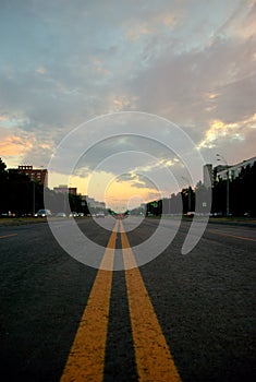 View of a new asphalt road with yellow markings closeup and sunset sky in the background.