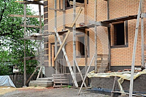 A view of a new brick house under construction with scaffolding,  uninstalled windows and unfinished porch. Clean construction