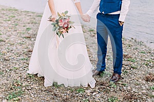 The view of the newlyweds legs standing on the beach. The view of the perfect wedding bouquet.