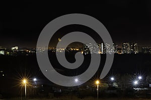 View of night city. Lights of multistoried buildings, bright street lamps. Urbanistic concept, city lights, moonlighting. Moon