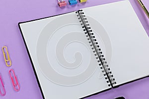 View of a notebook and colorful paperclips on plain purple background