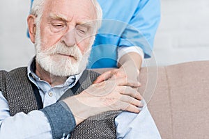 View of nurse standing behind senior man, putting hand on his shoulder